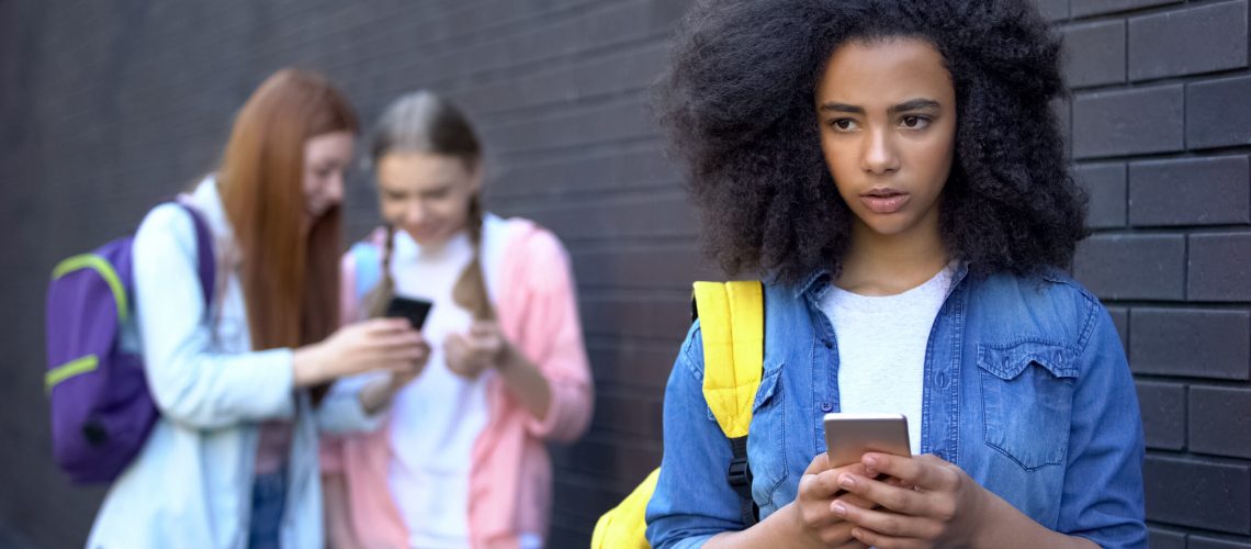 Sad african schoolgirl reading humiliating message, cyber bullying embarrassment