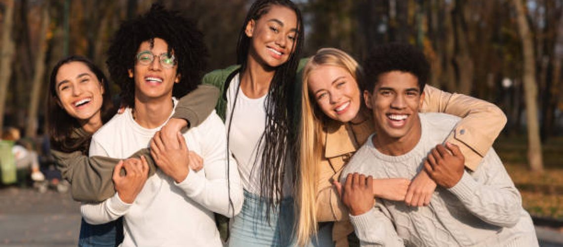 Positive group of multiracial young friends having fun at public park, hugging and smiling