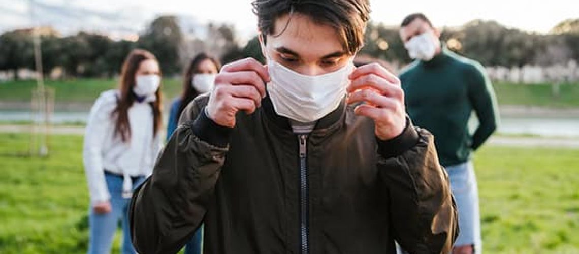 Group of teenagers friends at park wearing medical masks to protect from infections and diseases - Conceptual Coronavirus virus quarantine - Copy space - Multiracial people having fun together